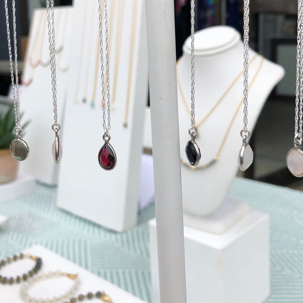 multiple gemstone pendants encased in sterling silver strung on sterling silver chains dangling from white necklace display