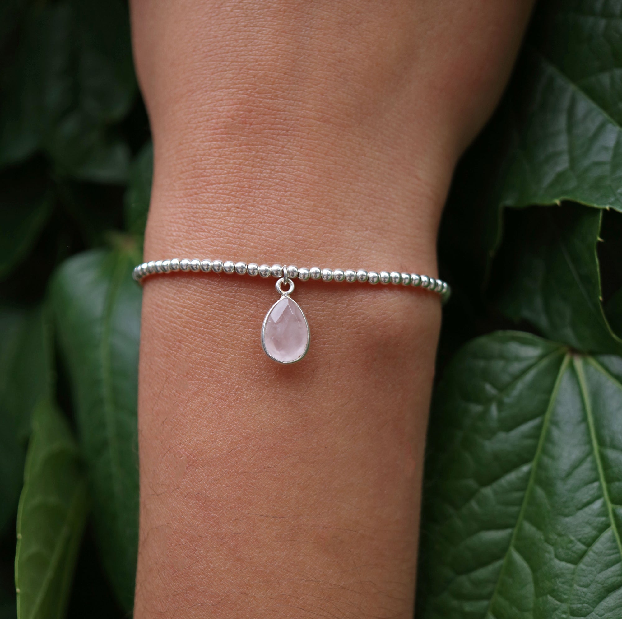 Dainty sterling silver beaded stretch bracelet featuring a natural rose quartz teardrop charm encased in sterling silver
