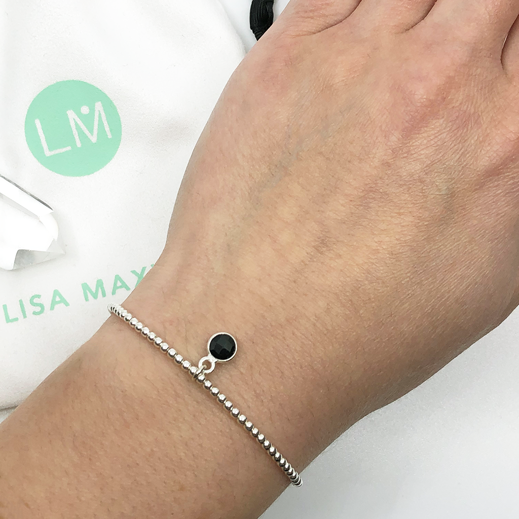 close up of woman wearing small onyx circle pendant encased in sterling silver dangling from a sterling silver beaded stretch bracelet 