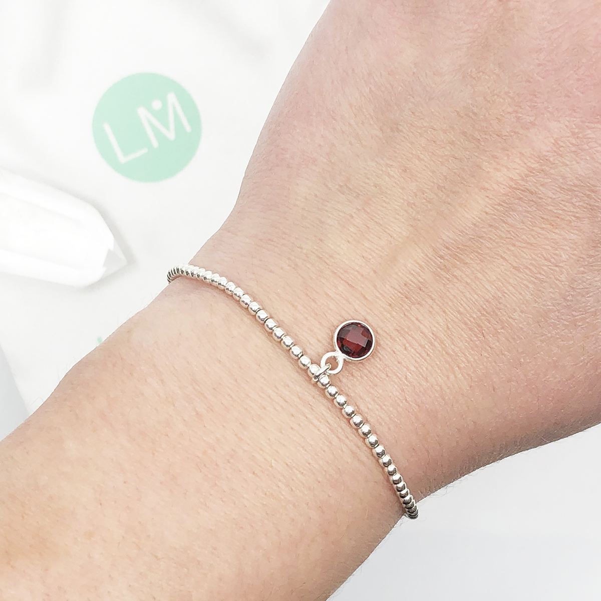 Dainty sterling silver beaded stretch bracelet featuring a natural garnet charm encased in sterling silver