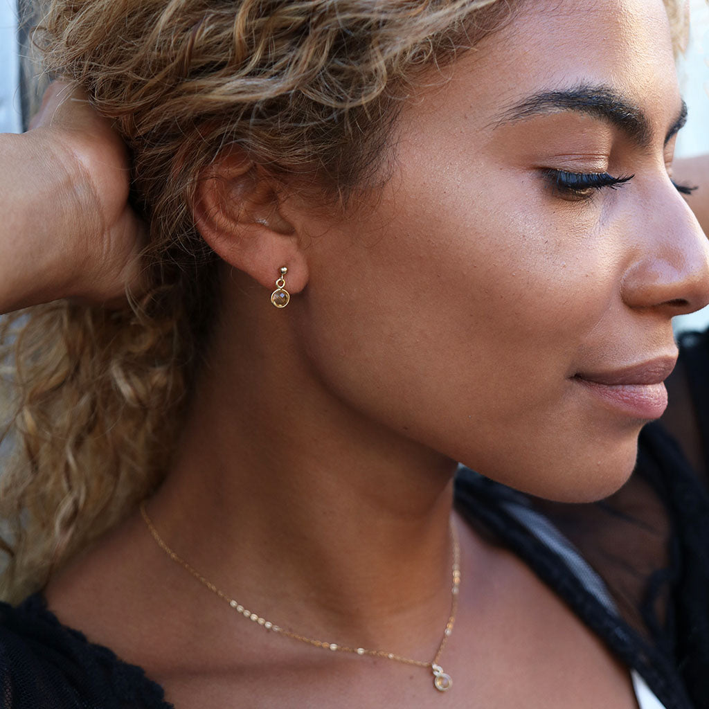 close up of woman wearing citrine crystal charm encased in gold hanging on a gold stud earring