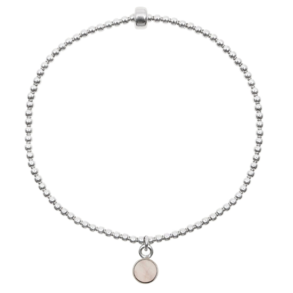Small rose quartz circle pendant encased in sterling silver dangling from a sterling silver beaded stretch bracelet and displayed on white background