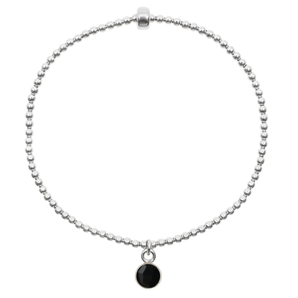 Small onyx gemstone circle pendant encased in sterling silver dangling from a sterling silver beaded stretch bracelet and displayed on white background