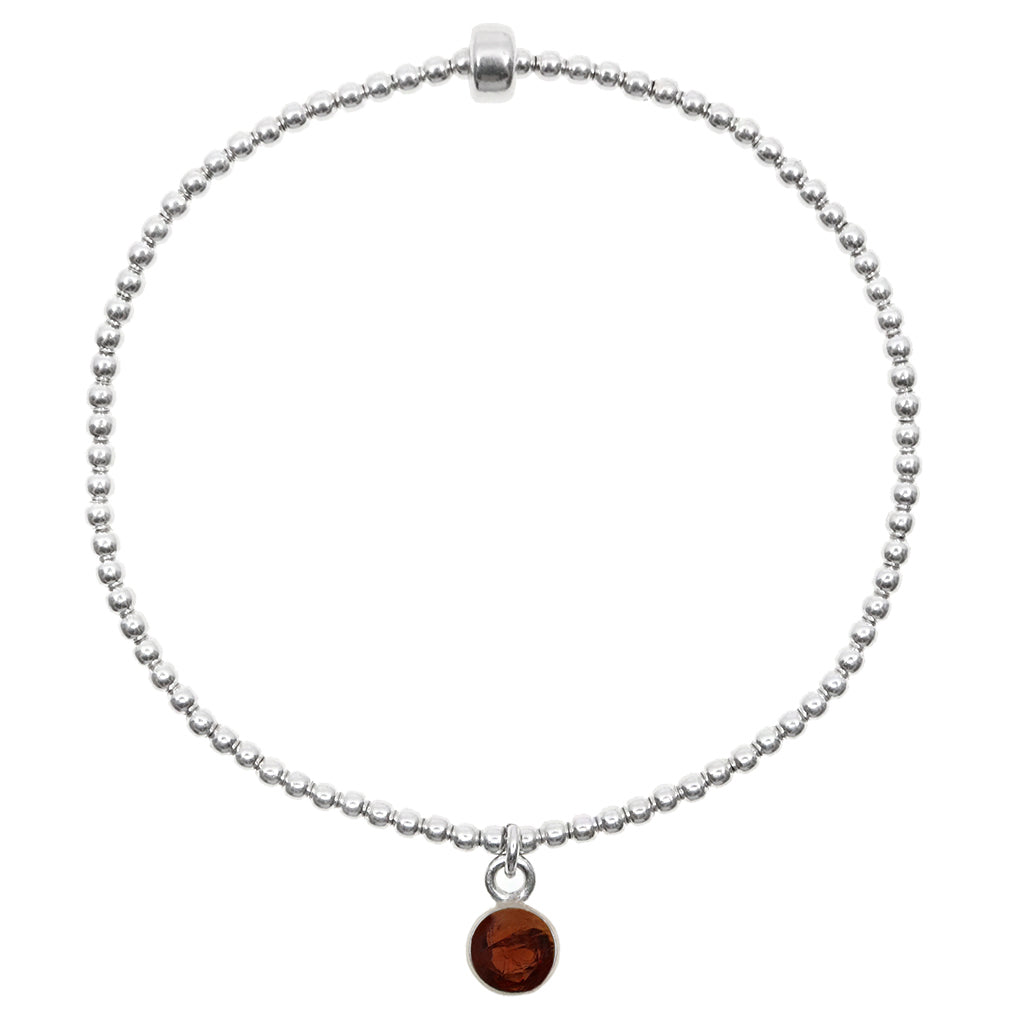 Dainty sterling silver beaded stretch bracelet featuring a natural garnet charm encased in sterling silver