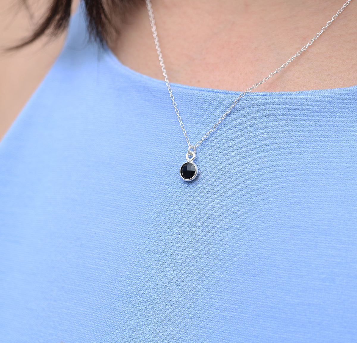 close up of woman wearing necklace featuring small onyx circle pendant encased in sterling silver strung on sterling silver rope chain
