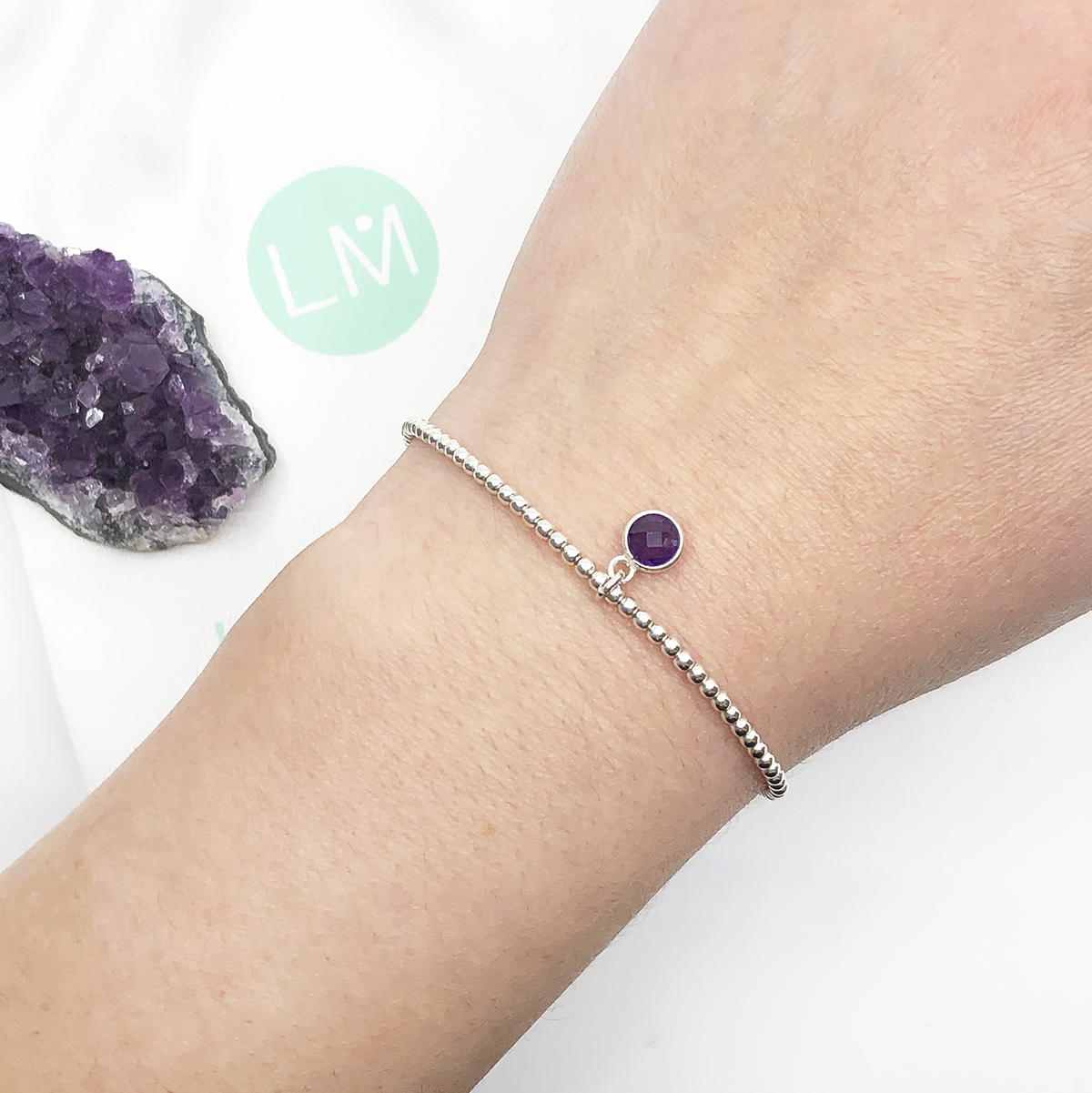 Dainty sterling silver beaded stretch bracelet featuring a natural amethyst charm encased in sterling silver.
