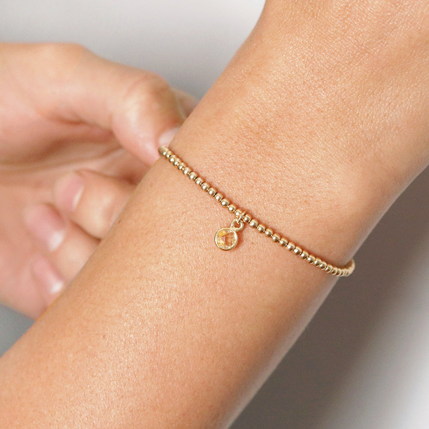 close up of woman's wrist showing Gold filled 2.5mm beaded stretch bracelet with 6mm citrine charm encased in gold over sterling silver